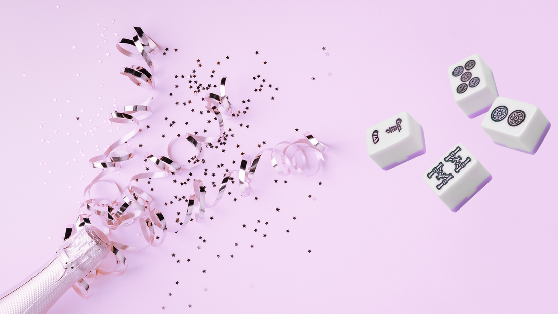 Mahjong tiles with pink confetti and ribbon on a soft pink background celebrating National Mahjong Day