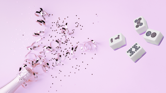 Mahjong tiles with pink confetti and ribbon on a soft pink background celebrating National Mahjong Day